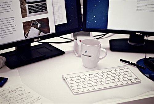 Desk setup with dual monitors, keyboard, and coffee mug